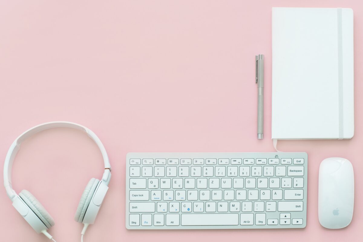 headphones, keyboard, mouse, notepad and pen sitting on a pink desk used for branding from a brand marketing agency