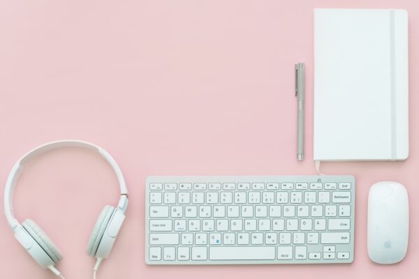 headphones, keyboard, mouse, notepad and pen sitting on a pink desk used for branding from a brand marketing agency